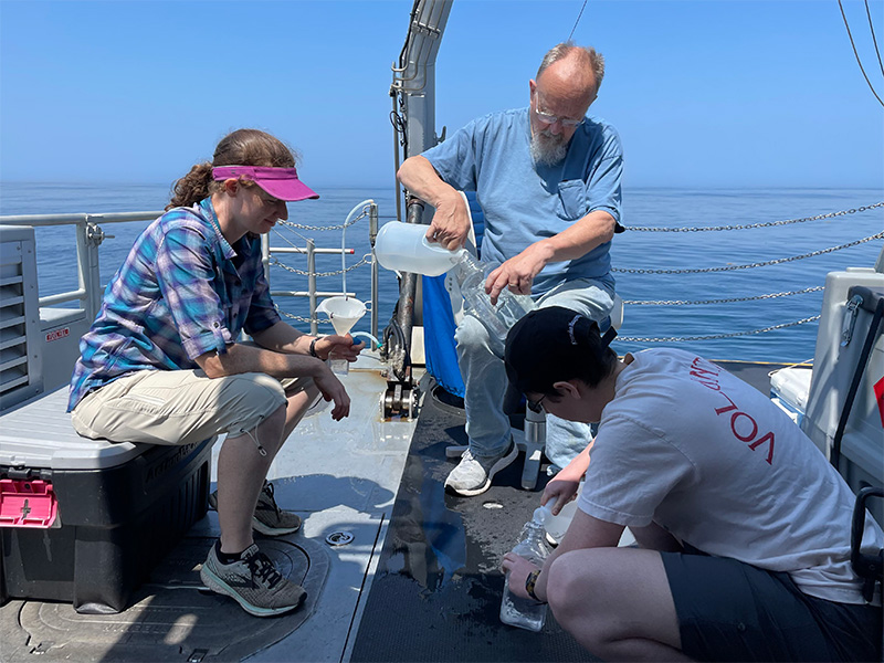 three people on the deck of a ship collecting water samples